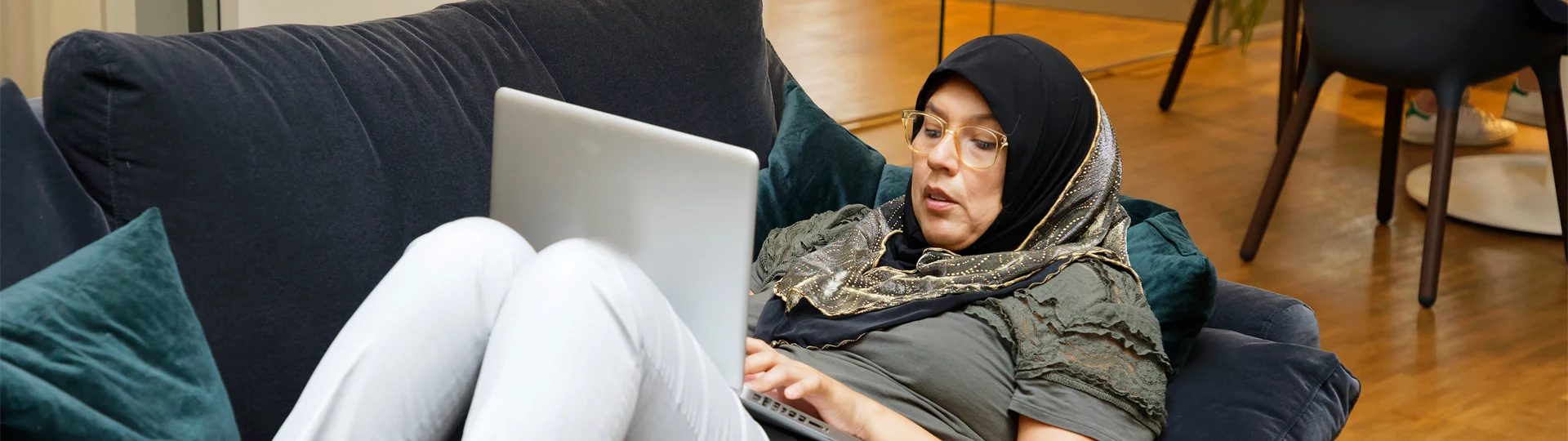 En person ligger i en soffa och arbetar med datorn.